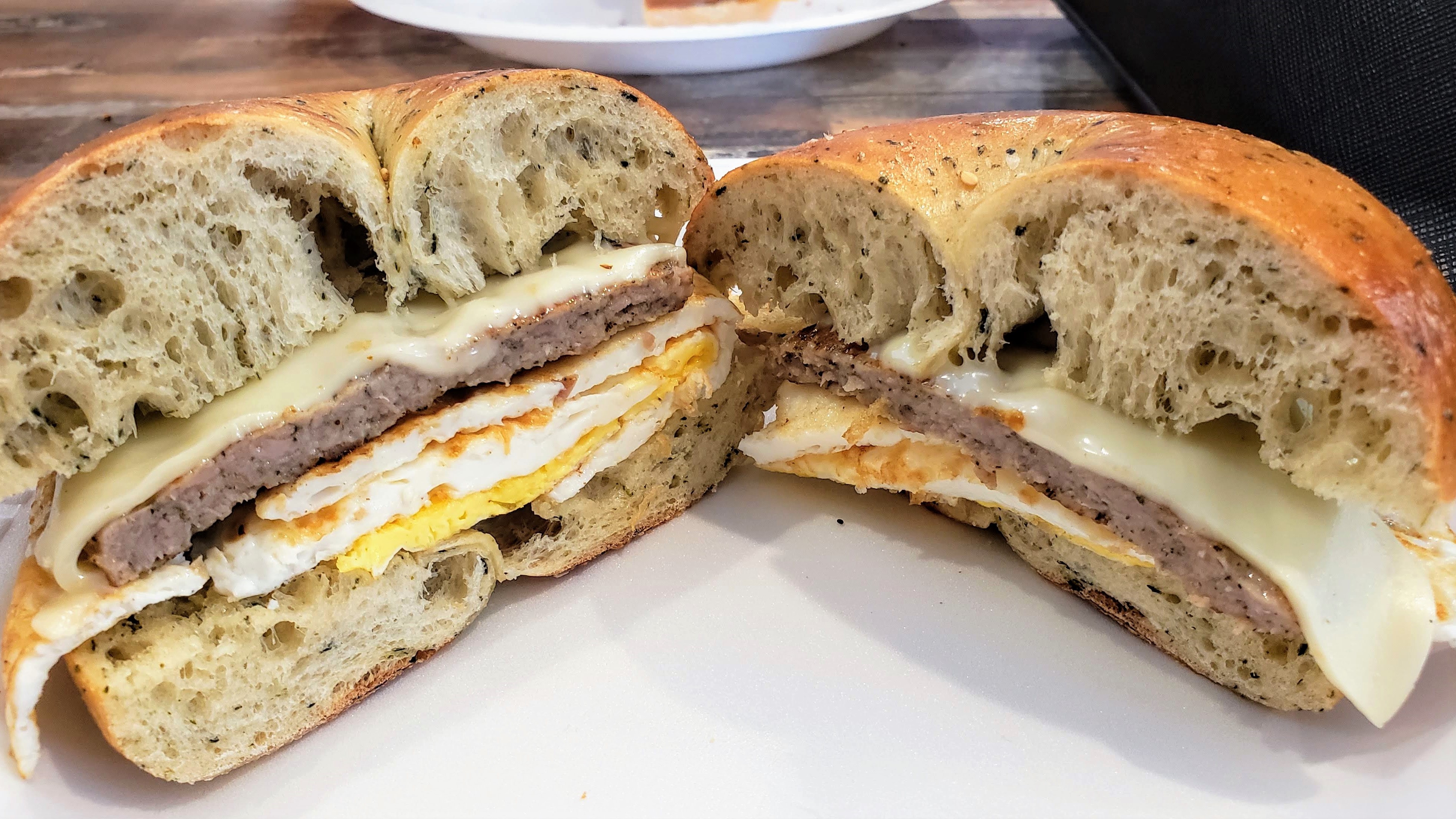 Breakfast sandwich cut open showing egg, sausage and cheese on a bagel